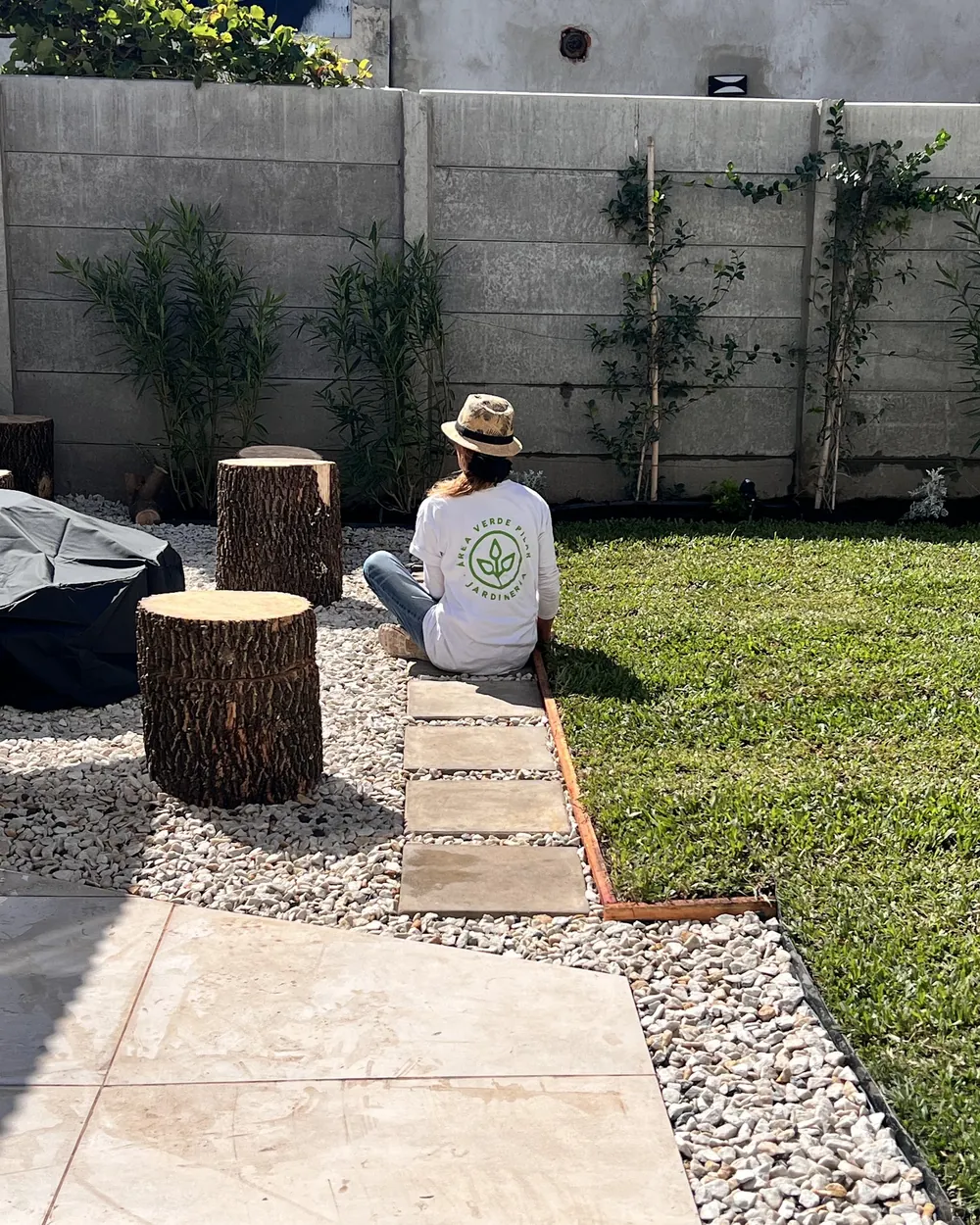 Jardín terminado por Área Verde: camino de lajas, piedra blanca, troncos como asientos y plantas trepadoras sobre la medianera